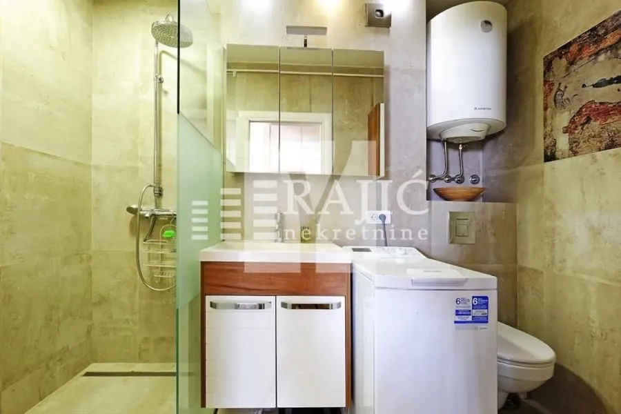 Modernly equipped bathroom with a walk-in shower, washbasin, and washing machine.