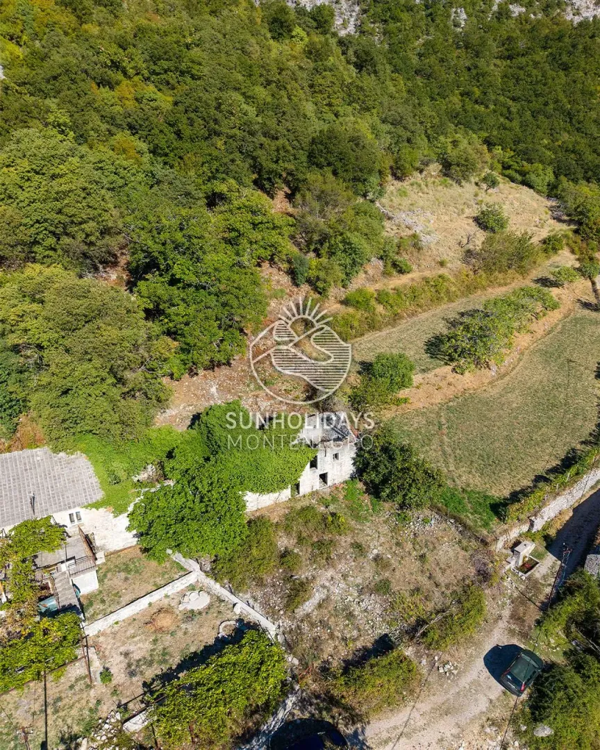 Pogled iz vazduha na staru kamenu kuću okruženu zelenilom.