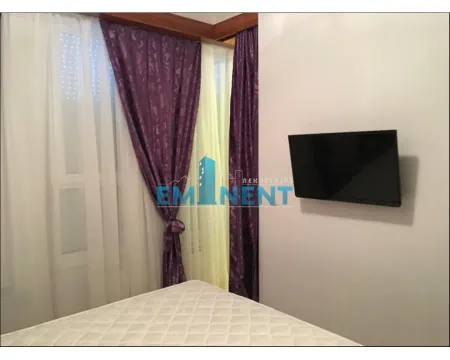 Bedroom with a bed, a window with purple curtains, and a wall-mounted TV. - image 8