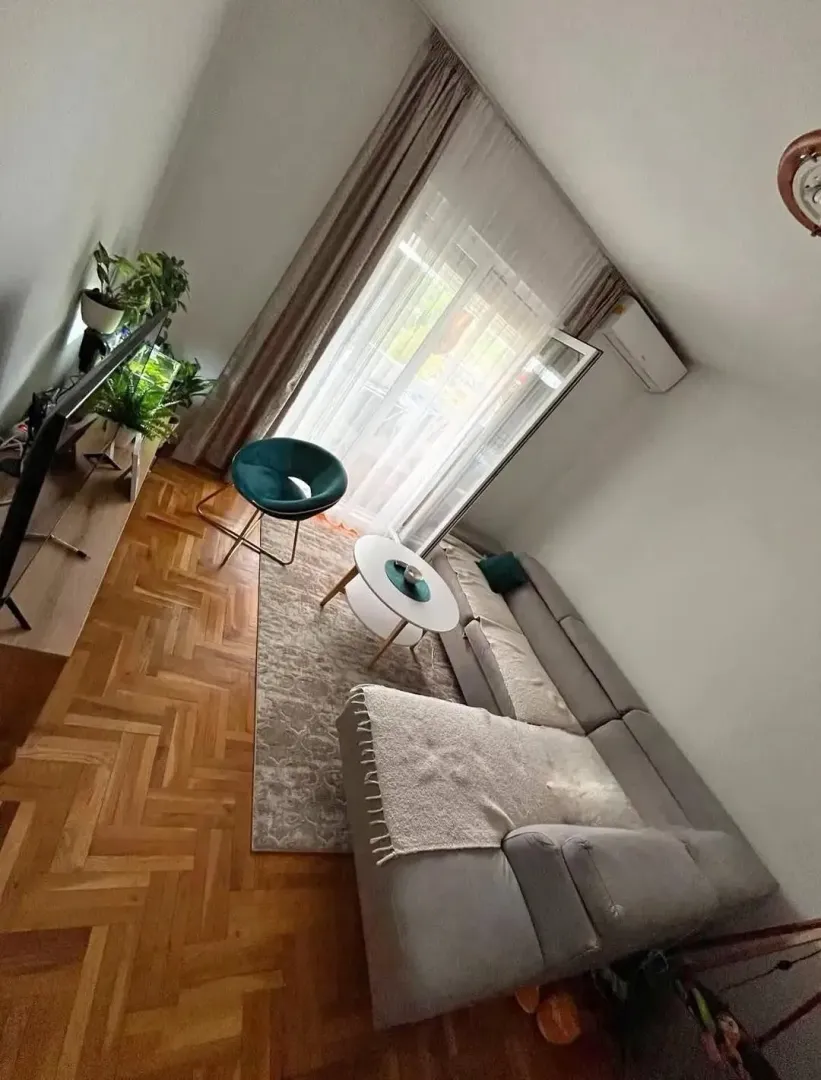 Dnevna soba sa ugaonom garniturom, stočićem i parketom na podu.