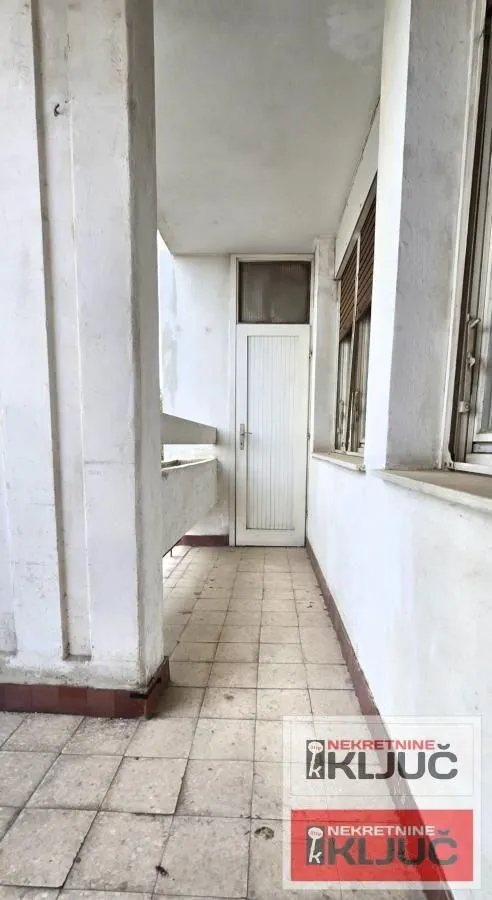 Nenamešten natkriveni balkon sa popločanim podom i vratima.