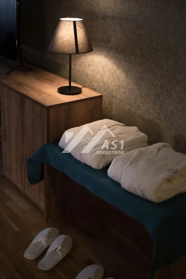 Detalj spavaće sobe sa uredno složenim peškirima, bade-mantilom i lampom na komodi.