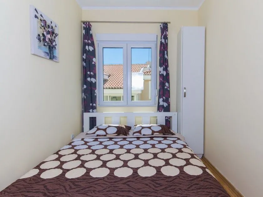 Manja spavaća soba sa bračnim krevetom, bijelim ormarom i prozorom.