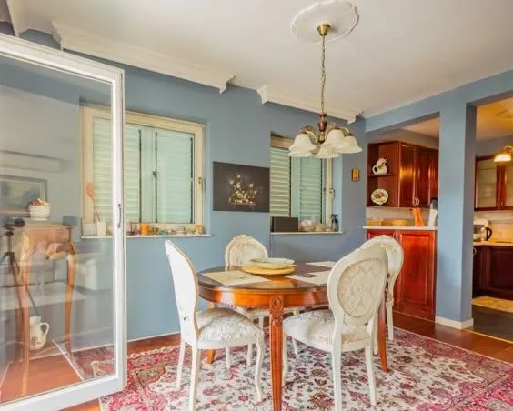 Dining area with a wooden table, chairs, and a rug, overlooking the kitchen.
