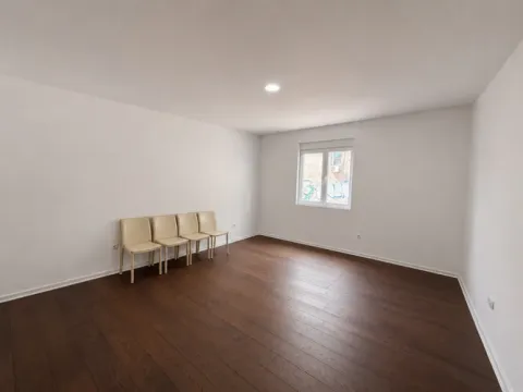 Prazna soba sa belim zidovima, tamnim parketom i nekoliko stolica uz zid. - image 7