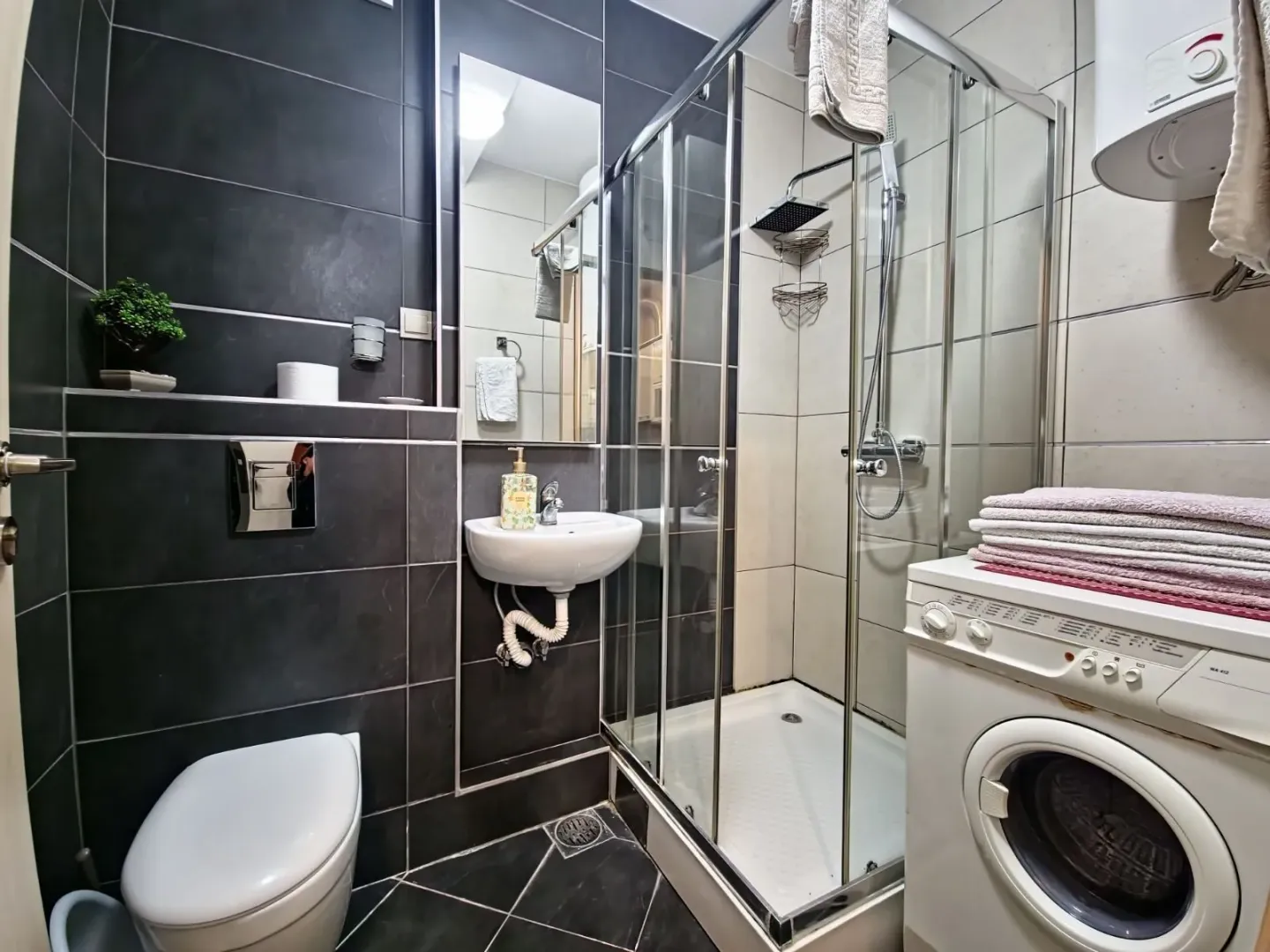 Moderno opremljeno kupatilo sa tuš kabinom, WC šoljom i veš mašinom.
