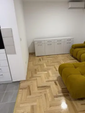 Deo dnevne sobe sa parketom, belom komodom i delom žute garniture. - image 2