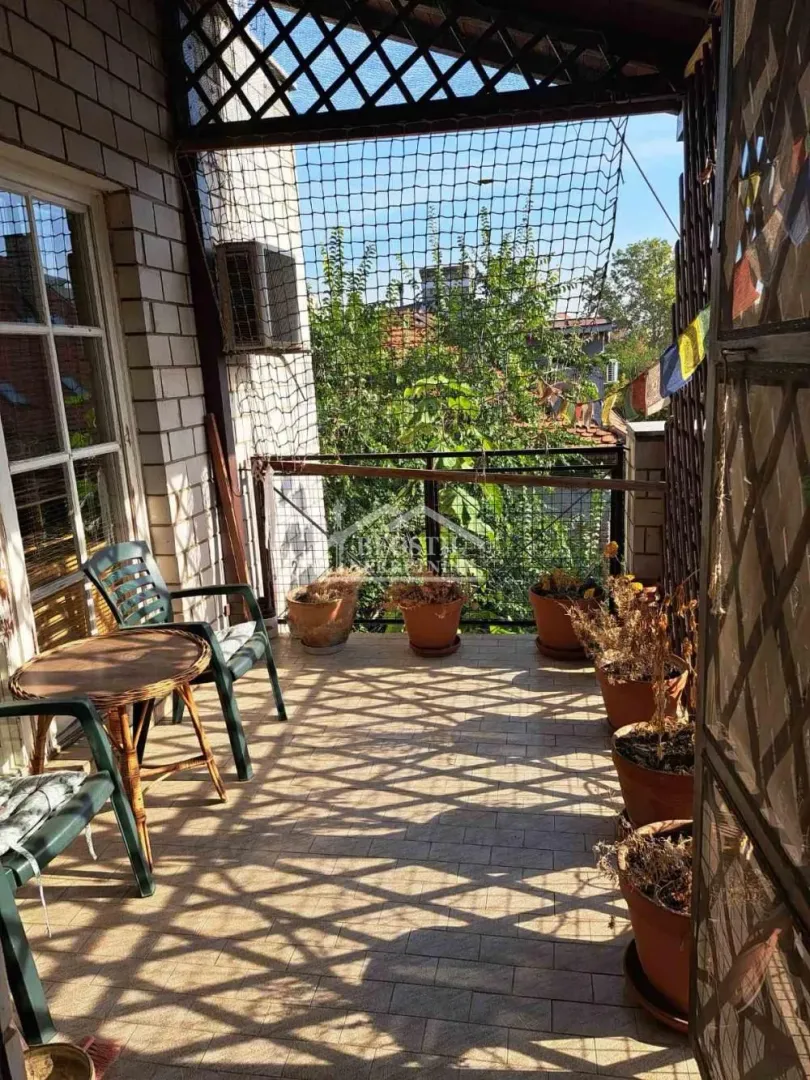 Covered balcony with seating furniture and potted plants.