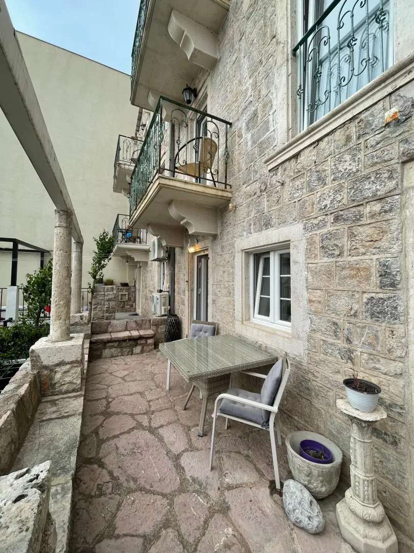 Stone building facade with balconies and a table with chairs in the yard.