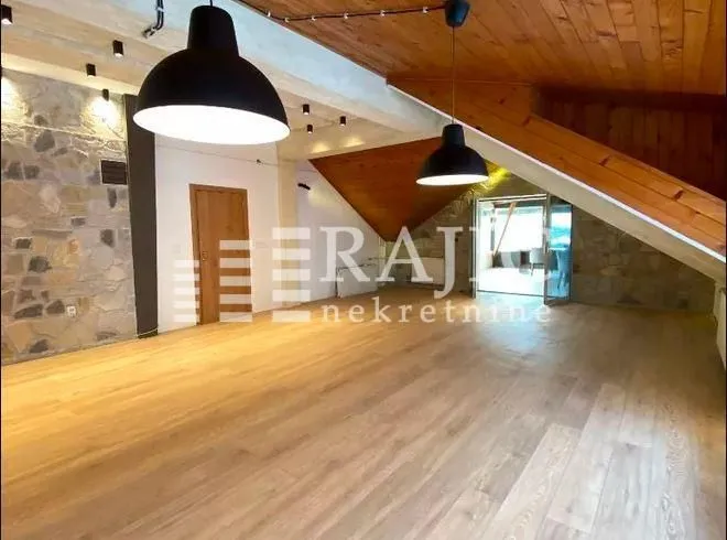 Spacious attic room with wooden flooring, wooden ceiling, and modern lighting fixtures.