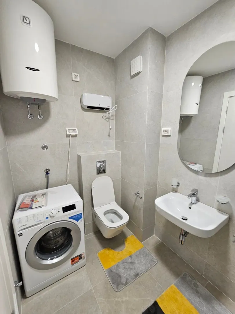 Moderne kupatilo sa tuš kabinom, umivaonikom i veš mašinom obloženo sivim pločicama.