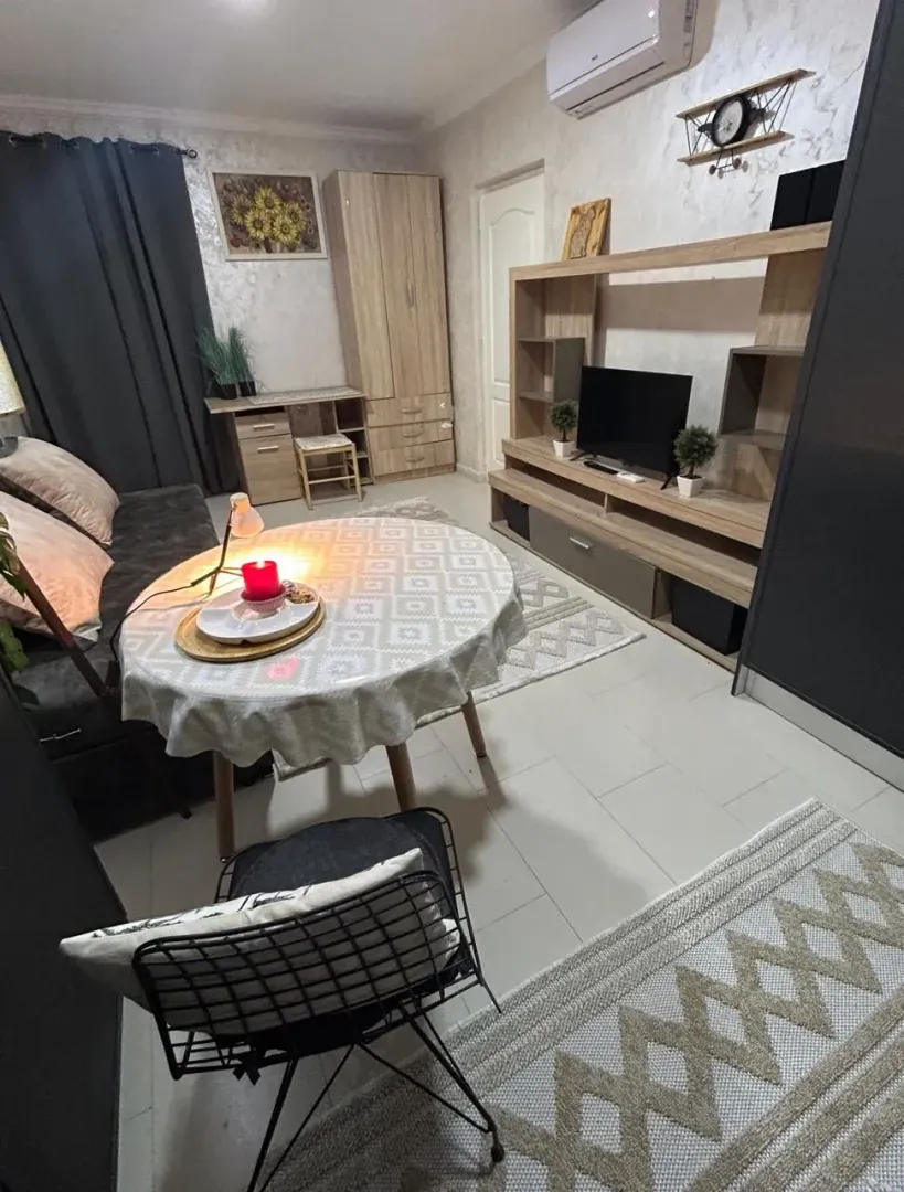 Furnished living room with a sofa, TV unit, and a small dining table.