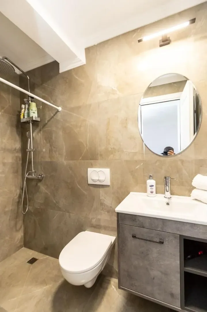 Moderne kupatilo sa tuš kabinom, umivaonikom i wc šoljom obloženo keramičkim pločicama u imitaciji kamena.