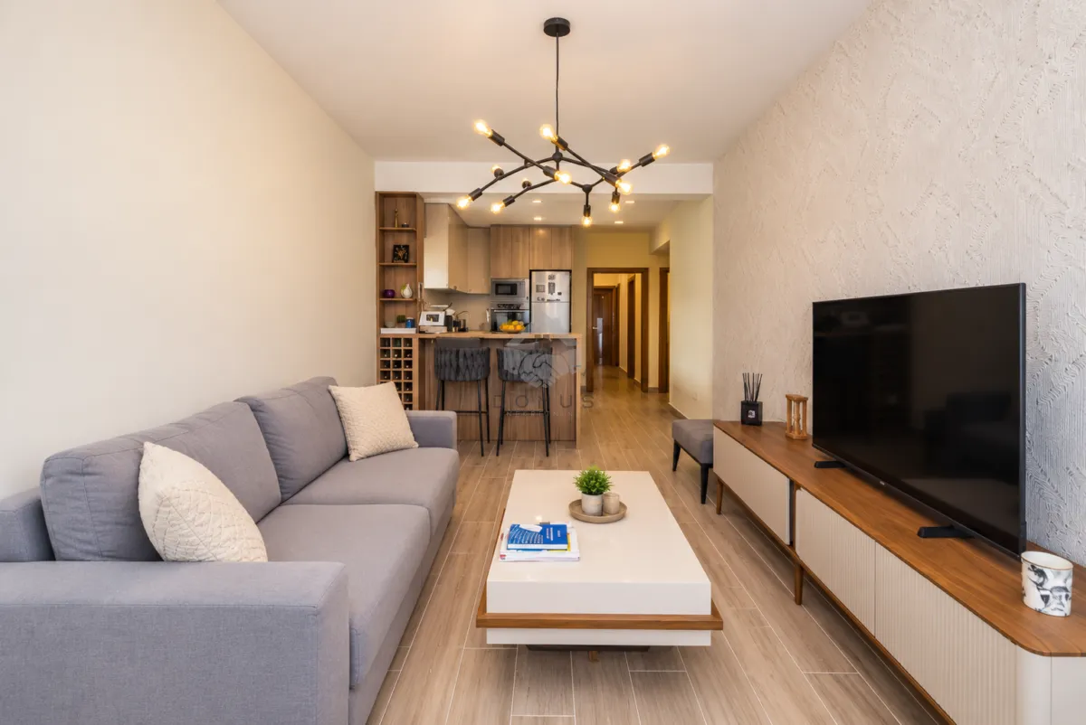 Living room with a sofa, TV, and a view of the kitchen in the background.