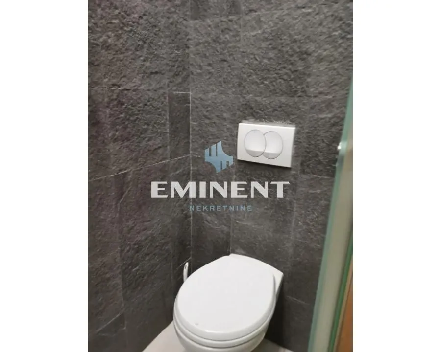 A view of a modernly equipped toilet with dark tiles.