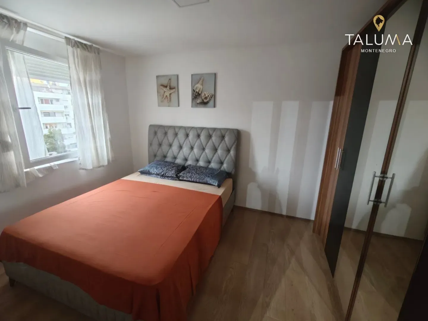 Spavaća soba sa bračnim krevetom, prozorom i velikim ormarom sa ogledalom.
