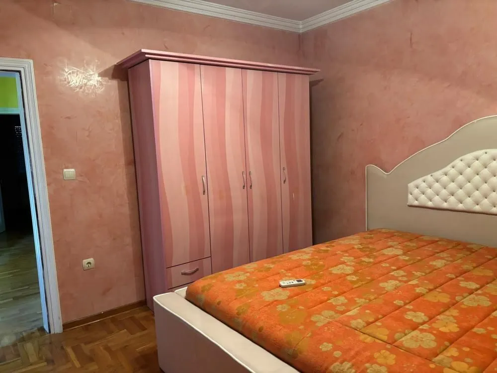 Bedroom with a double bed, large pink wardrobe, and reddish walls.