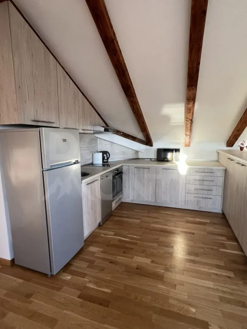 Attic kitchen with wooden beams and light-colored cabinetry.