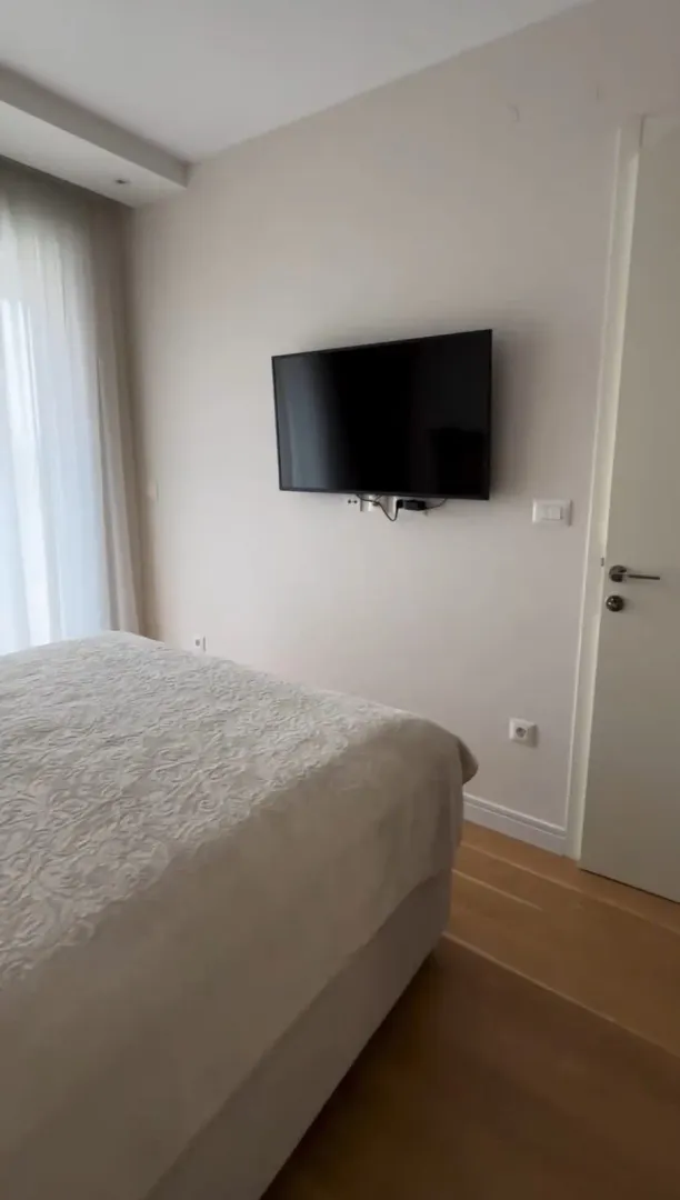 Uređena spavaća soba sa bračnim krevetom i zidnim televizorom.