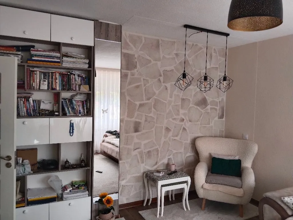 Dnevna soba sa foteljom, bibliotekom i zidom obloženim dekorativnim kamenom.