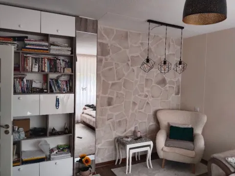 Dnevna soba sa foteljom, bibliotekom i zidom obloženim dekorativnim kamenom. - image 4