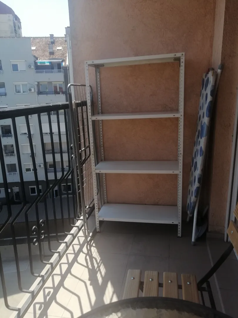 Small furnished balcony with a metal shelf, drying rack, and ironing board.