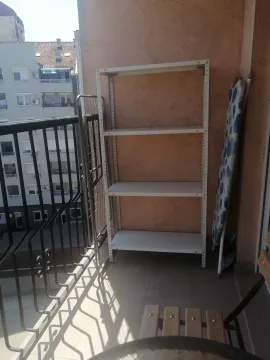 Small furnished balcony with a metal shelf, drying rack, and ironing board. - image 6
