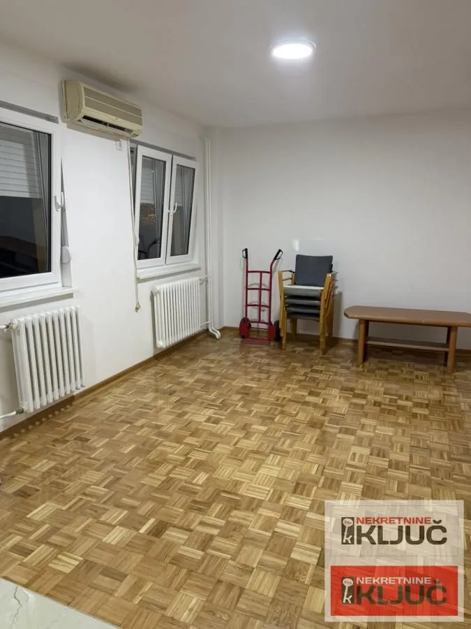 Prazna soba sa parketom na podu i belim zidovima.