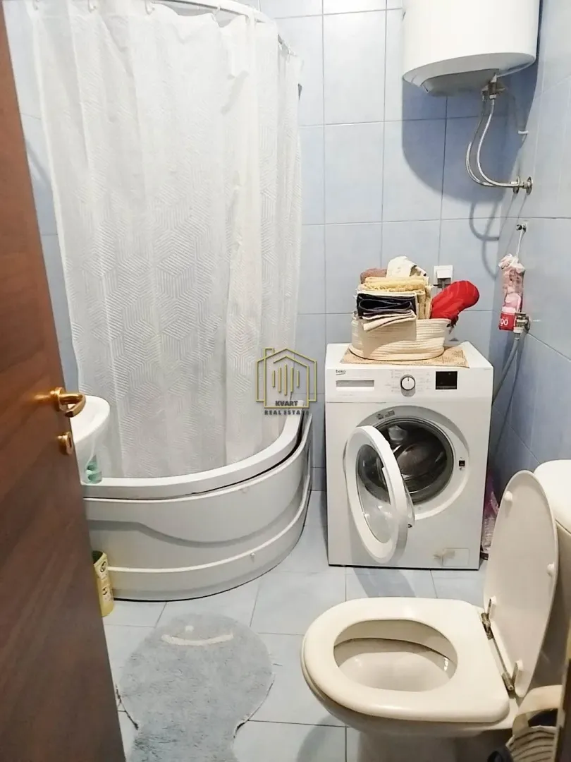 Manje kupatilo sa tuš kabinom, WC šoljom i veš mašinom.