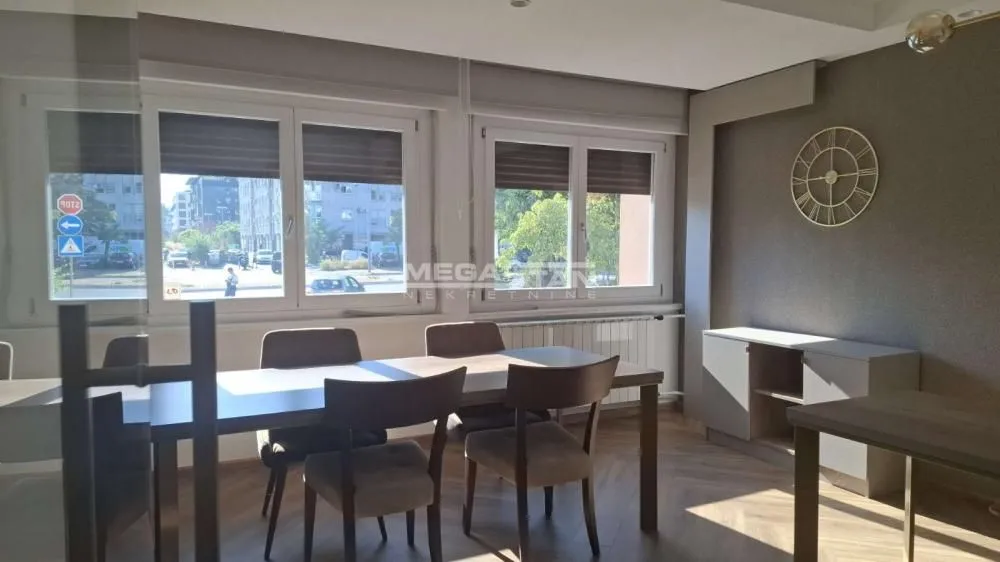 Dining area with a table, chairs, and large windows overlooking the street.
