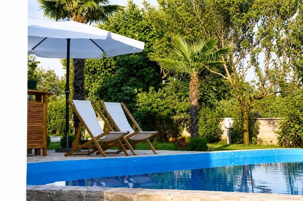 Swimming pool with sun loungers and an umbrella in a landscaped yard.