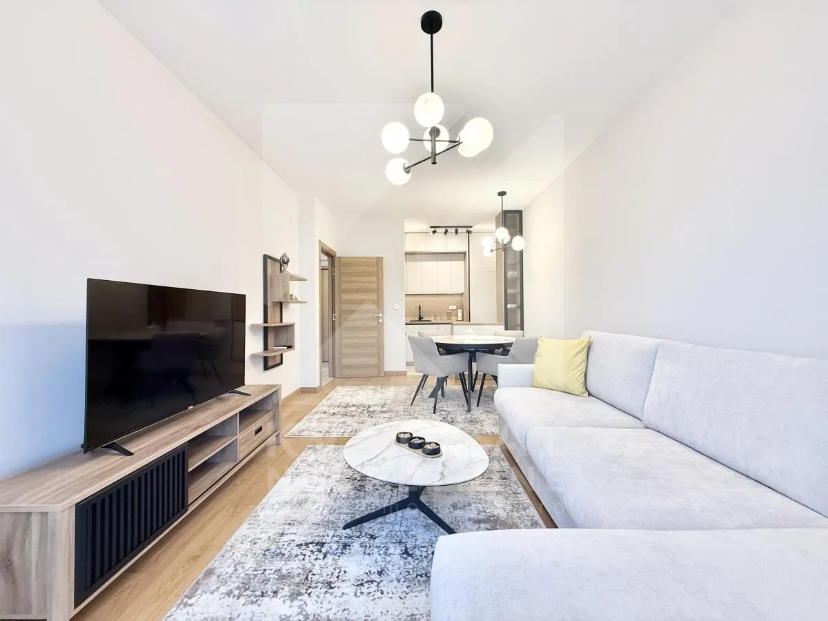 Living room with a sofa, TV unit, and a view towards the dining area and kitchen.