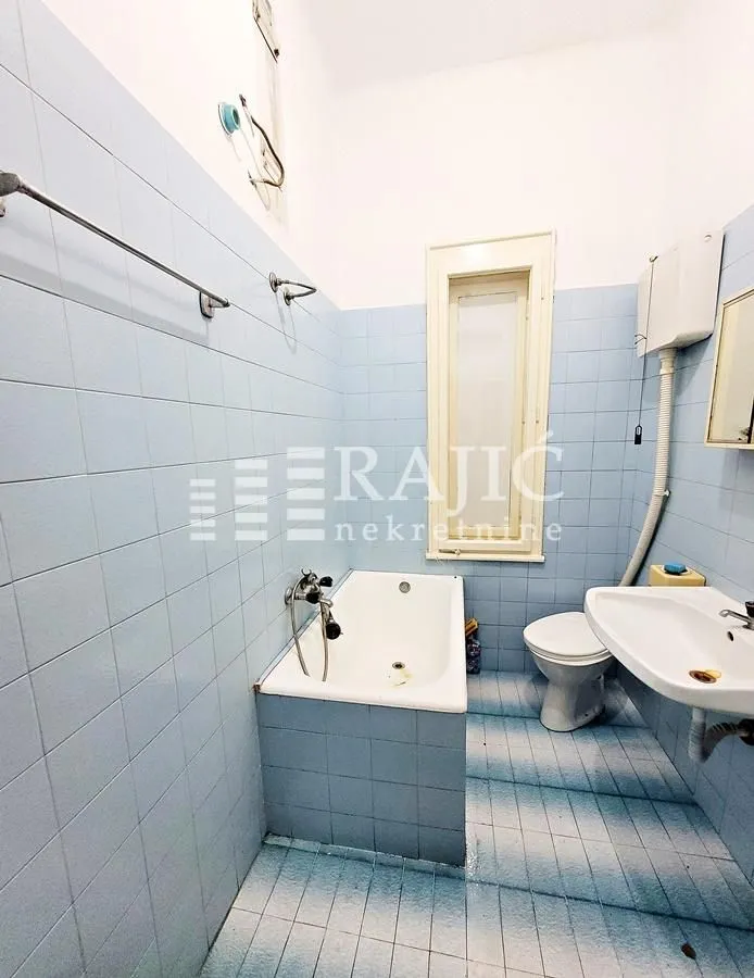 Smaller bathroom with blue tiles, bathtub, sink, and toilet.