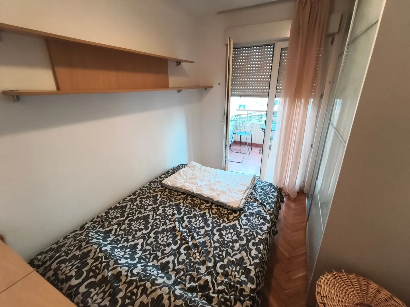 Manja spavaća soba sa krevetom, zidnim policama i izlazom na terasu.