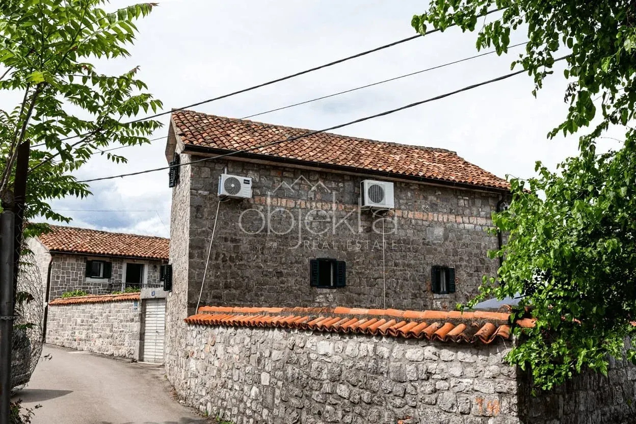 Pogled na tradicionalnu kamenu kuću sa dvorištem i ulicom u prvom planu.