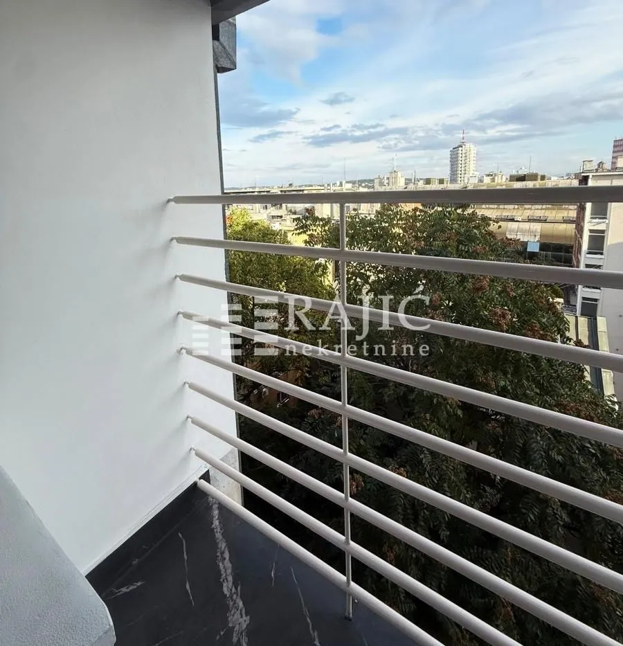 Manji svijetli balkon sa ogradom i pogledom na grad.