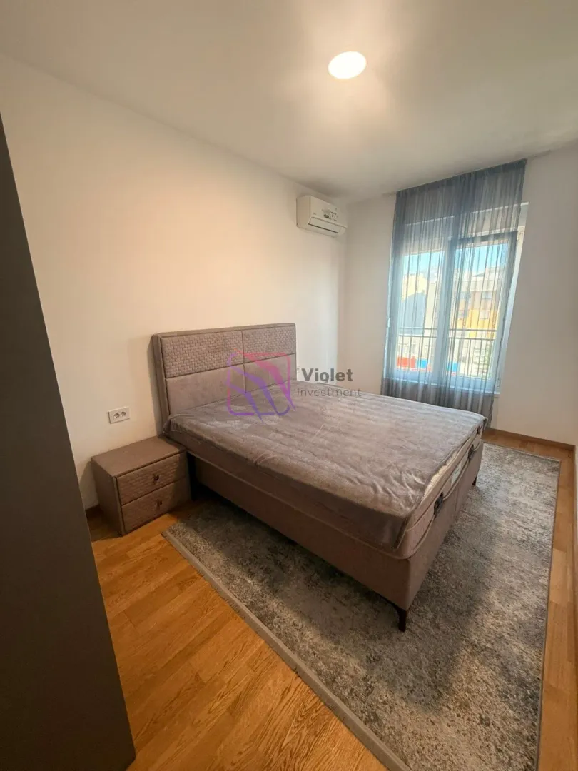 Spavaća soba sa bračnim krevetom, noćnim stočićem i prozorom sa zavjesama.