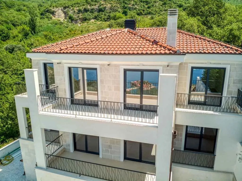 Pogled iz vazduha na fasadu trospratne kuće sa terasama i crvenim krovom.