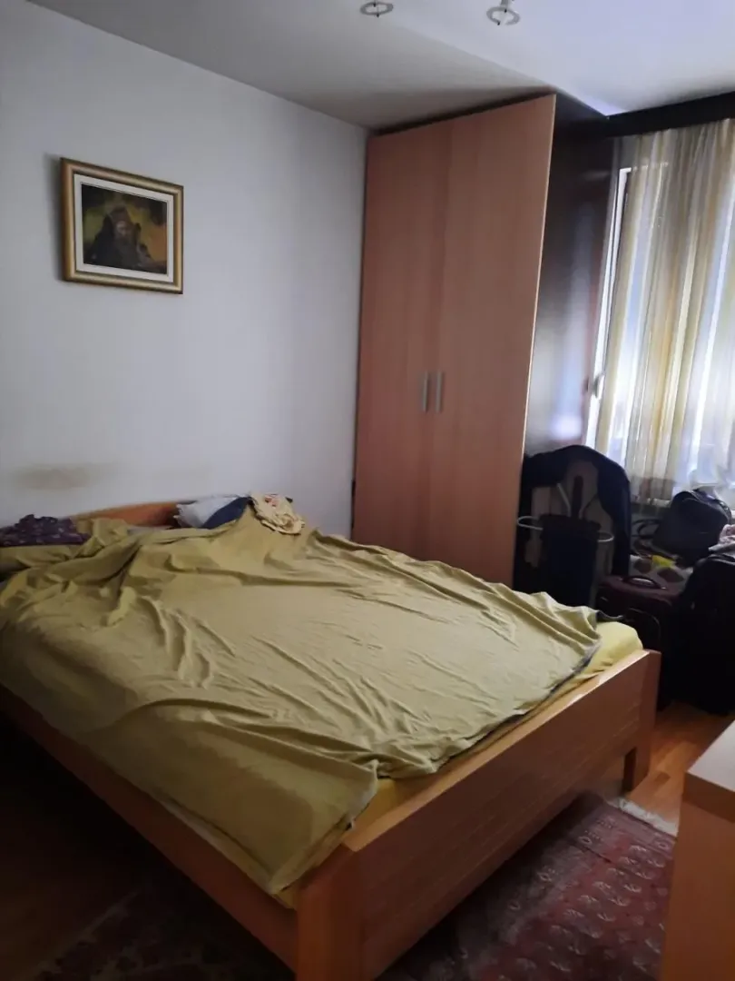 Furnished bedroom with a double bed, wooden wardrobe, and a painting on the wall.