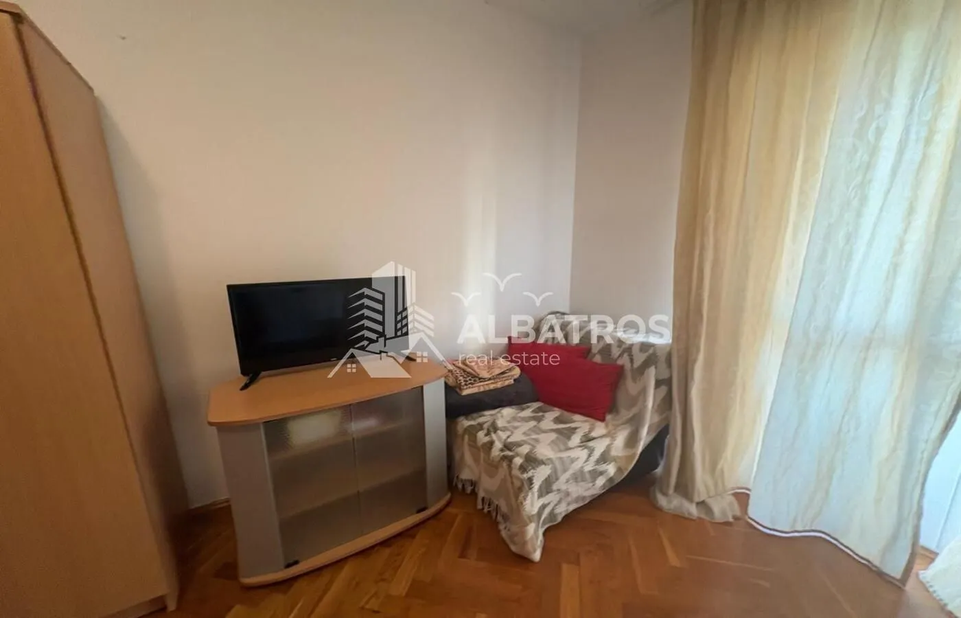 Manja spavaća soba sa krevetom, TV komodom i parketom na podu.