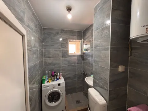Manje kupatilo obloženo sivim pločicama sa veš mašinom, umivaonikom i toaletom. - image 4
