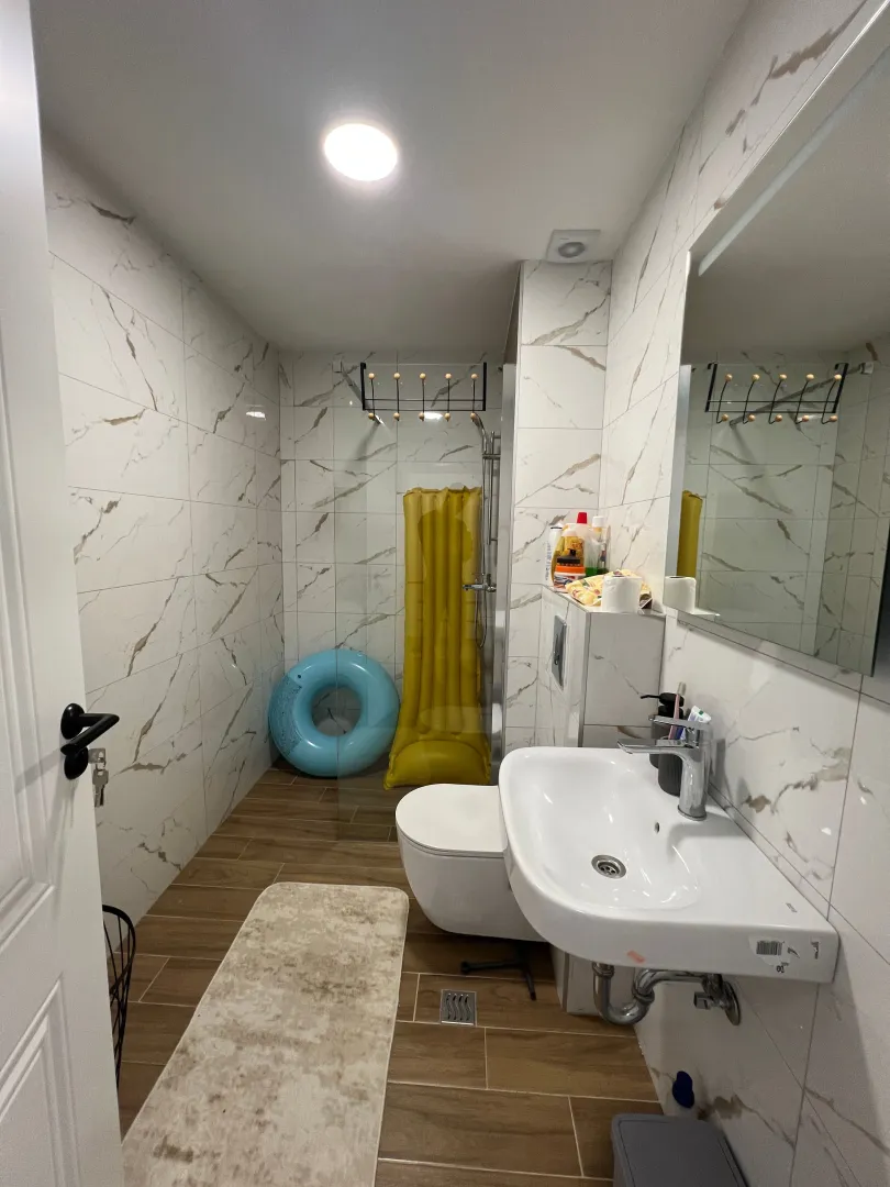Modern bathroom tiled with marble-pattern tiles featuring a washbasin and a walk-in shower.