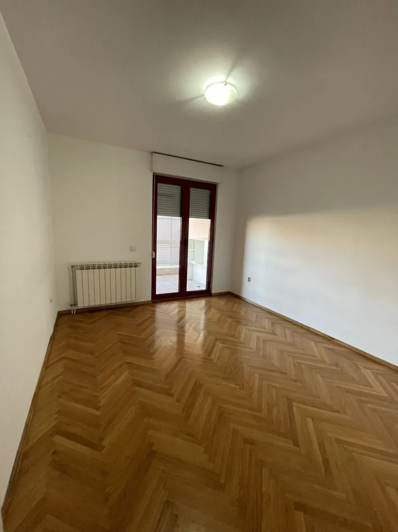 A bright empty room with parquet flooring and balcony doors.