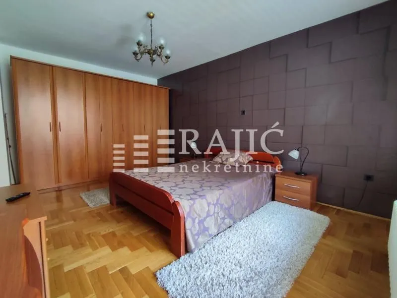 Furnished bedroom with a double bed, large wooden wardrobe, and parquet flooring.