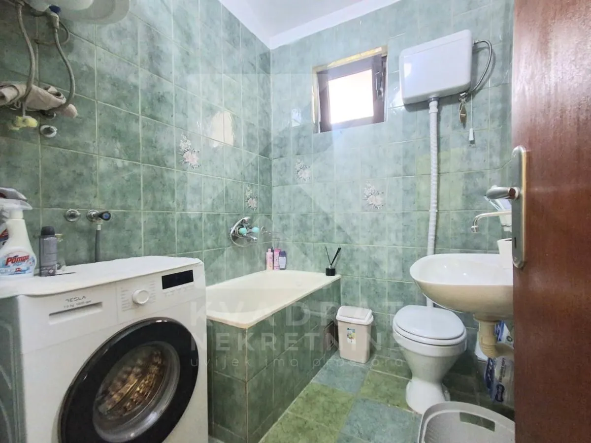 Kupatilo obloženo zelenim pločicama sa kadom, umivaonikom, WC šoljom i veš mašinom.