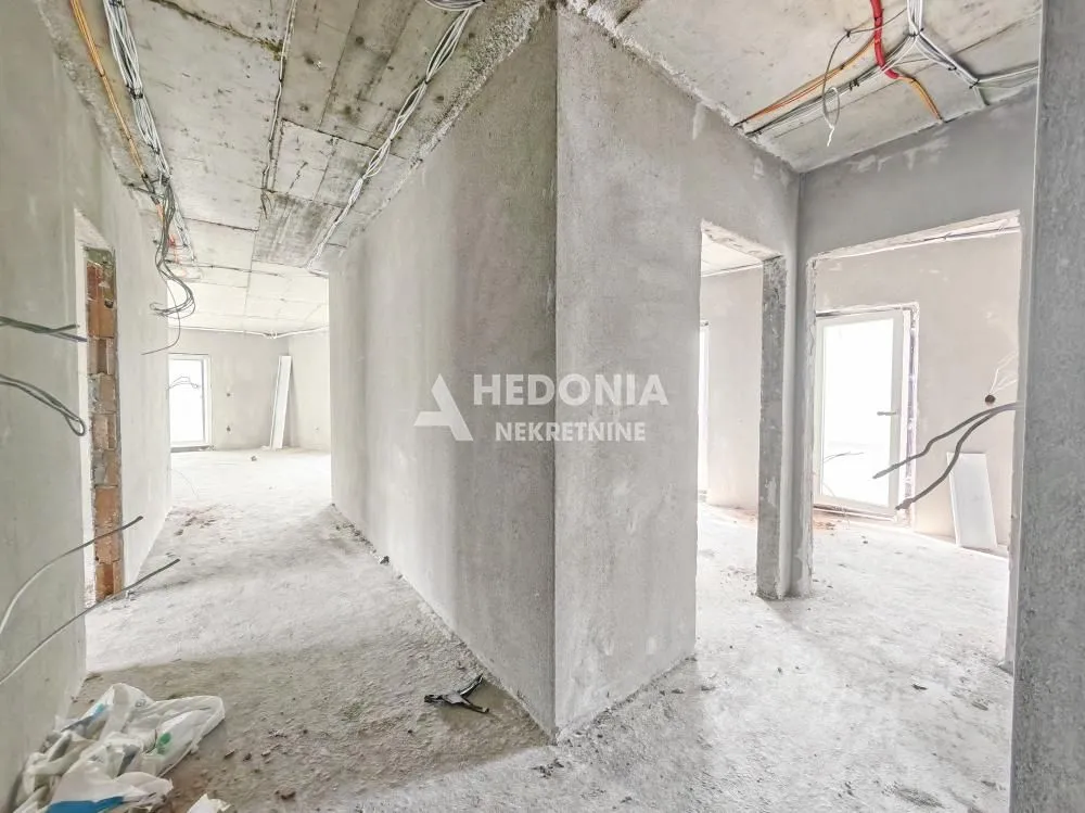 Pogled na unutrašnjost nekretnine u izgradnji sa malterisanim zidovima i betonskim plafonom.