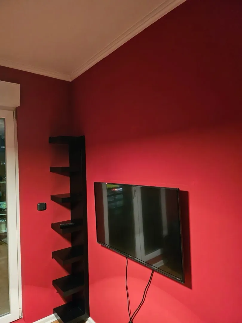 Crveni zid sa montiranim televizorom i crnom ugaonom policom.