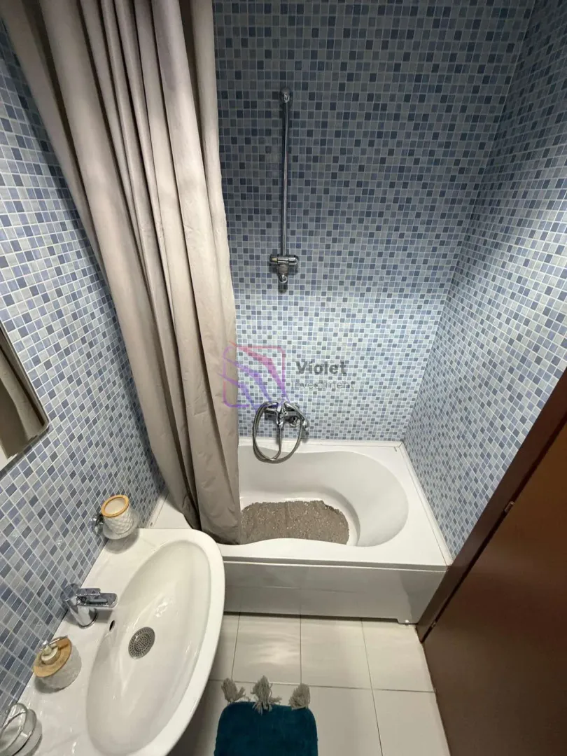 Bathroom with a bathtub, shower and washbasin tiled in blue tones.