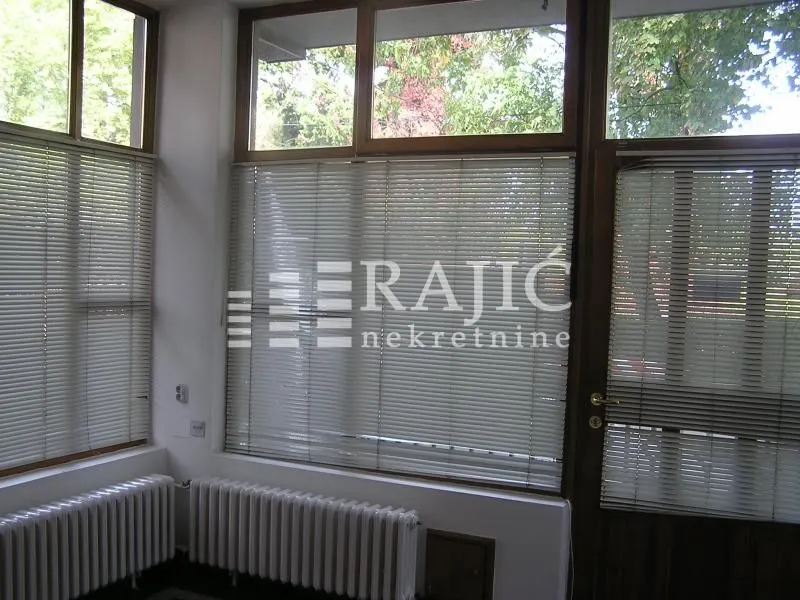 Bright room with large windows, blinds, and radiators underneath.