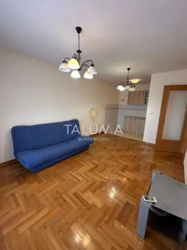 Dnevna soba sa plavim kaučem i parketom, sa pogledom na kuhinju u pozadini. - image 3